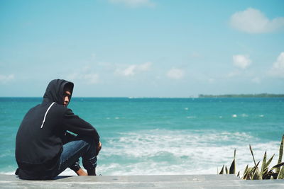 Man sitting on beach against sky