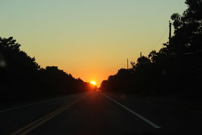 Road amidst silhouette trees against clear sky during sunset