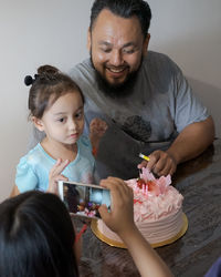 Woman photographing man and daughter cutting cake