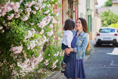 Mother and little handsome baby boy looking at bush with white roses