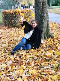 Portrait of young woman sitting on tree during autumn