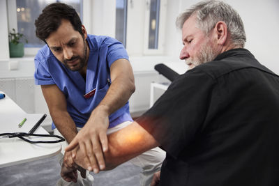 Male doctor examining senior patient's elbow