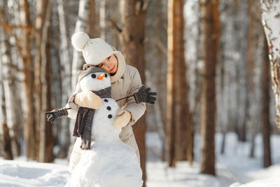 Portrait of teenage girl embracing snowman in forest