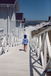 Boy child in a striped blue sailor jacket walks on the street among white wooden houses by the sea