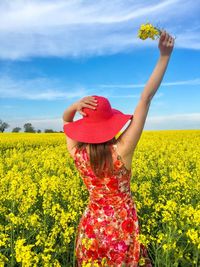 Close-up of young woman with yellow flowers in field against sky