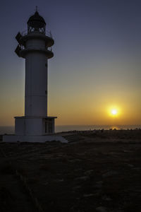 Lighthouse on silhouette beach against sky during sunset