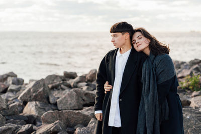 Lesbian women embracing while standing on rock against sea and sky