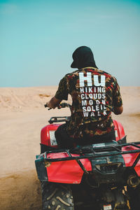 Rear view of man riding motorcycle in desert against sky