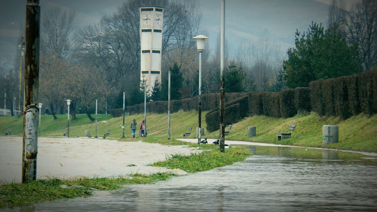 water, grass, built structure, architecture, the way forward, road, building exterior, street, sky, footpath, incidental people, tree, nature, day, tranquility, wet, transportation, outdoors, pathway, fence