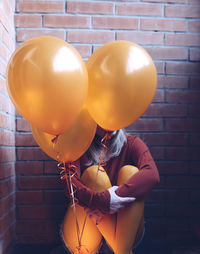 Woman with balloons sitting against wall