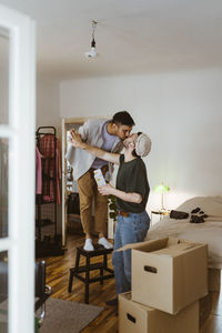 Man standing on stool kissing boyfriend at home