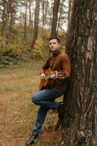 Young man playing guitar while sitting in forest