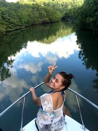 Portrait of woman showing peace sign while sitting on yacht bow in lake