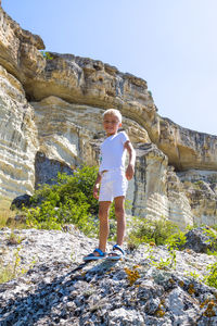 Full length of boy standing on rock against clear sky