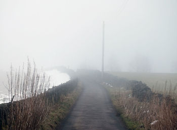 Road amidst field against sky during foggy weather