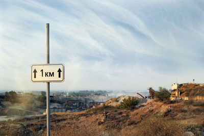 Road sign on field against sky