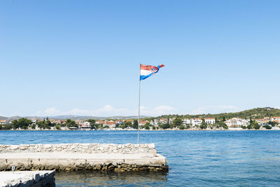 Flag by sea against clear blue sky