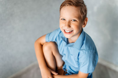 A cute boy in a blue shirt is sitting and smiling