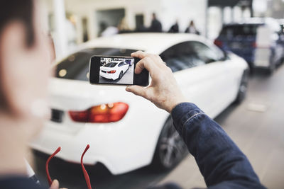 Senior woman photographing new car through mobile phone at showroom