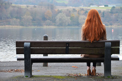 Rear view of woman sitting on bench against lake