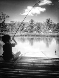 Boy sitting by lake against sky