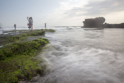 Friends standing on rock by sea against sky