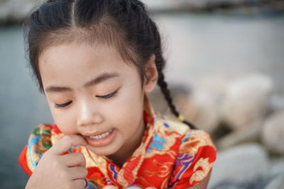 Close-up of girl looking down while sitting on rocks against sea