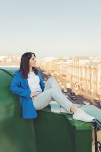 Portrait of young woman sitting on railing against clear sky