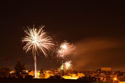 Firework display over illuminated buildings against sky at night
