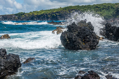 Sea waves splashing on rocks against sky