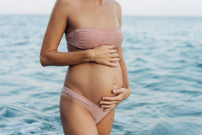 Large pregnant female belly of an anonymous woman on the background of the sea.