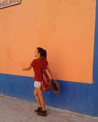 Rear view of young woman walking on footpath by orange wall
