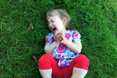 High angle view of little girl laying on grassy field having tantrum