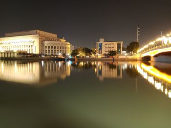 Illuminated buildings by lake against sky in city at night