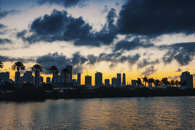 Silhouette buildings by sea against sky during sunset