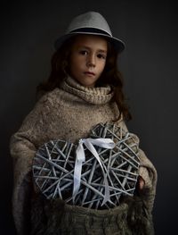 Portrait of cute girl holding heart shape while standing against gray background