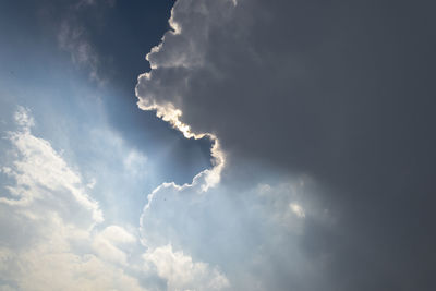 Low angle view of sunlight streaming through clouds