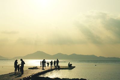 Group of silhouette people on jetty along sea