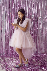 Beautiful girl with big eyes in a pink dress stands against the background of new year's tinsel