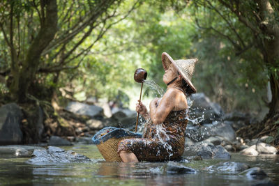 Senior woman taking bath while sitting on rock in river