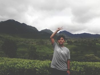 Portrait of teenage boy showing peace sign while standing against mountains