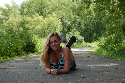 Portrait of young woman lying on road in forest