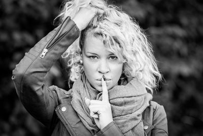 Portrait of young woman with finger on lips standing at park