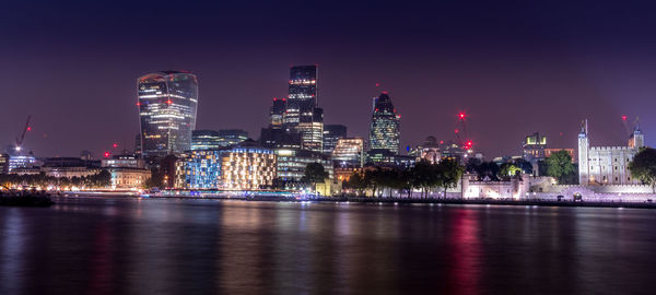 Illuminated buildings by river against sky at night