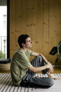 Side view of thoughtful young woman sitting on carpet at home