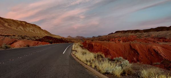 Empty road leading towards mountains against sky