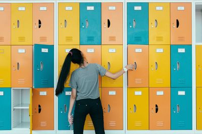 Rear view of young woman against multi colored lockers