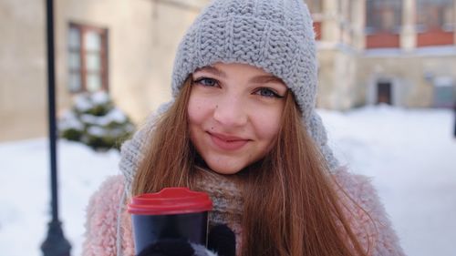 Portrait of young woman holding coffee cup while standing outdoors