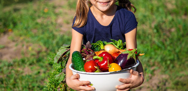 Midsection of girl carrying fresh vegetables in bowl