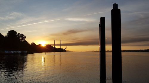 Silhouette of wooden post in sea against sky during sunset